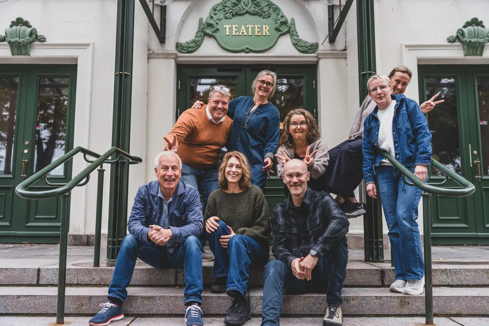 Nio av delägarna i Klara Kompetenser skrattar tillsammans på trappan till teatern i Karlstad