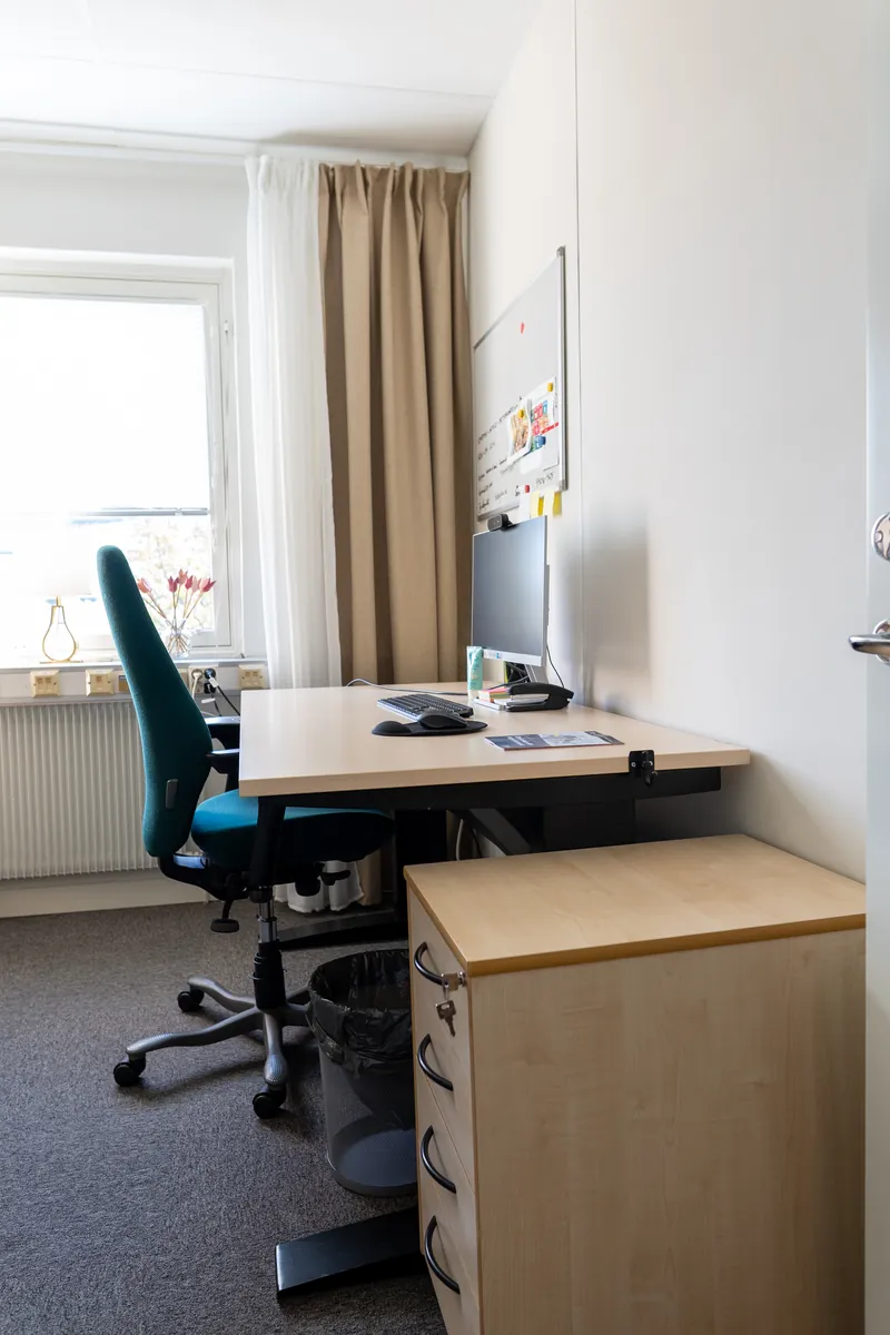 Skrivbord med skärm, grön kontorsstol och hurts i det lilla kontorsrummet